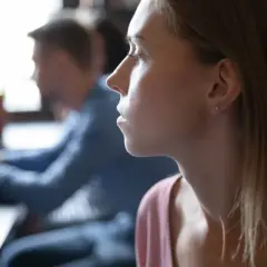 Kobieta z zamyśloną miną, być może zmagająca się z myślami typowymi dla osobowości anankastycznej, siedzi przy stole.