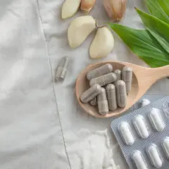 Kapsułki z magnezem na łyżce, obok czosnku i liści. Zastanawiasz się, ile magnezu dziennie?