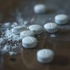 Białe tabletki, niektóre pokruszone, leżą na drewnianym blacie. To niebezpieczny fentanyl narkotyk.