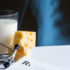 Szklanka mleka, ser, jajko i stetoskop na tle zdjęcia rentgenowskiego. Zdrowa dieta bogata w wapń jest kluczowa dla mocnych kości.