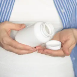 Kobieta w ciąży trzyma białą buteleczkę i jej nakrętkę. Rozważa, czy wziąć paracetamol w ciąży.