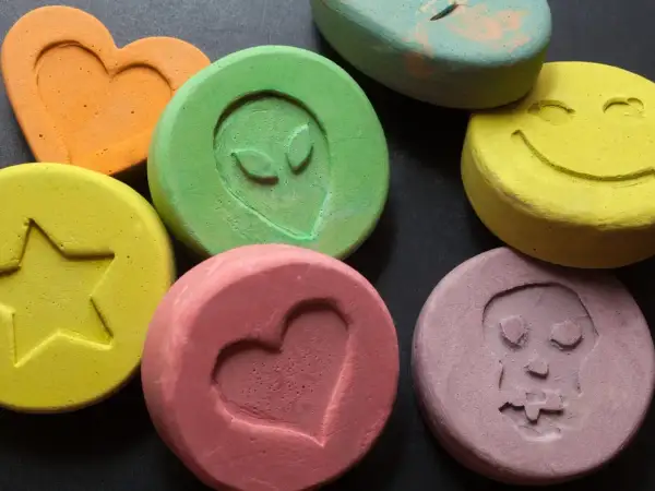 Kolorowe tabletki z symbolami: serce, gwiazda, kosmita, uśmiech, czaszka. To mogą być tabletki MDMA.