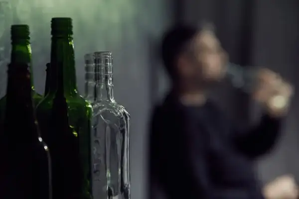 Puste butelki, jedna z nich jest przezroczysta, a obok niewyraźna postać pije alkohol. To może być jego dawka śmiertelna.