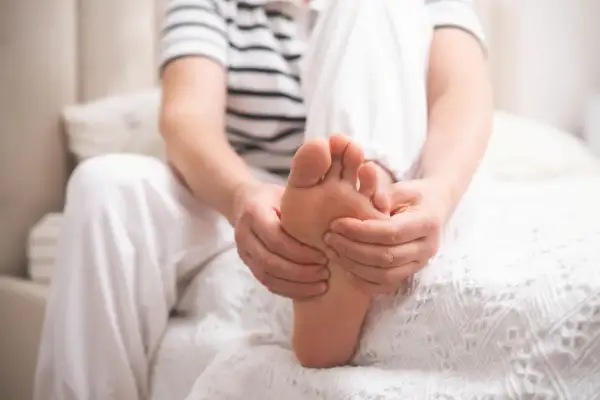 Osoba masuje stopę, odczuwając ból związany z neuropatią cukrzycową.